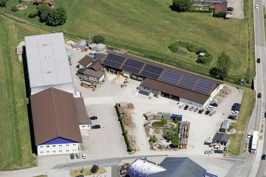 Luftaufnahme eines Gewerbeobjekts mit mehreren Gebäuden, Solarmodulen, Parkplätzen und Außenlagerflächen, geeignet für Industrie- oder Geschäftsbetriebe.