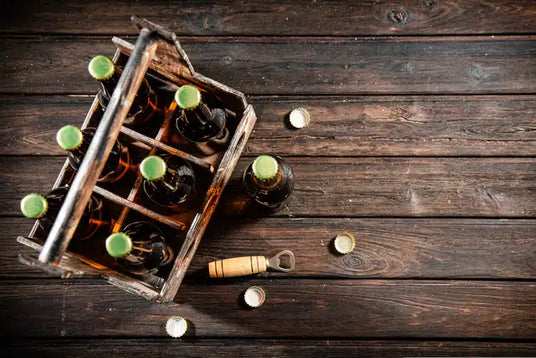 Ein Holzkasten, gefüllt mit verschlossenen Bierflaschen, begleitet von einem Flaschenöffner und losen Flaschenverschlüssen.