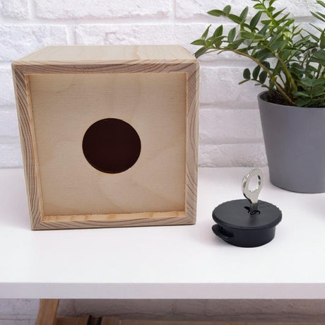 Holzwürfel mit runder Öffnung und schwarzem Stopfen mit Schlüssel.