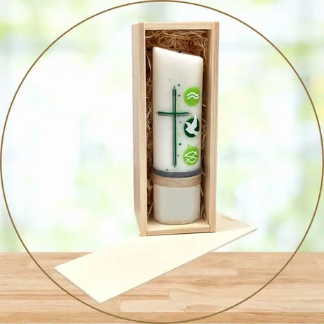 Weiße Kerze mit grünen christlichen Symbolen in einer Holzkiste.