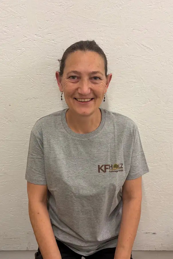 Graues kurzärmeliges T-Shirt mit einem braunen ’kfh’-Logo und kleinem Grafikmotiv auf der linken Brust