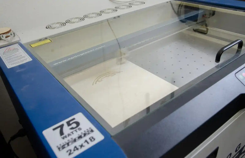 Ein Lasergravur- oder Schneidegerät mit einem transparenten Deckel, ausgestattet mit einem Arbeitsbereich mit einem perforierten Bett.
