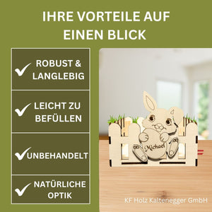 Eine hellfarbene hölzerne Hasenfigur mit einem personalisierten Namen, der auf ihrem Bauch graviert ist, sitzend in einem passenden hölzernen Zaun-Design.