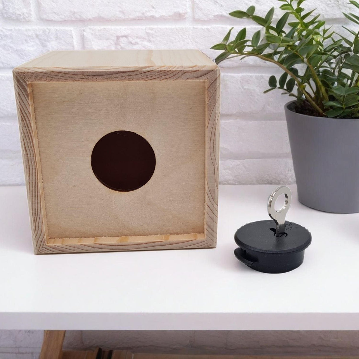 Holzwürfel mit runder Öffnung und schwarzem Stopfen mit Schlüssel.