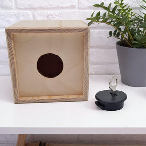 Holzwürfel mit runder Öffnung und schwarzem Stopfen mit Schlüssel.