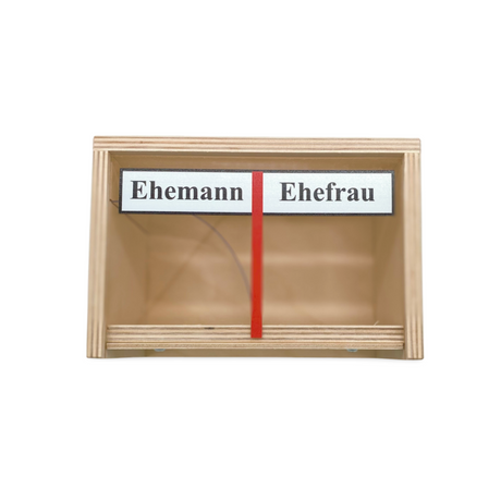 Eine Holzkiste mit zwei Fächern, die mit ’Ehemann’ und ’Ehefrau’ beschriftet und durch eine rote Trennwand getrennt sind.
